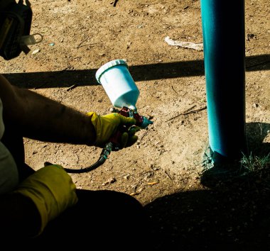 Belediyenin çalışanları parktaki bir oyun parkındaki boya borularını boyuyor. Bir balondan sprey boya.