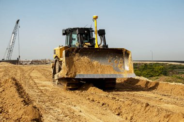 Asfalt yol inşaatı. Buldozer, otoyolun tabanındaki kil toprağını daraltıyor ve düzleştiriyor. Bir yaz gününde toprak işleri.