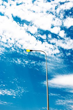 Gün boyunca lamba direğindeki ışıklar açık. Beyaz bulutlu mavi gökyüzüne karşı parlayan lamba.