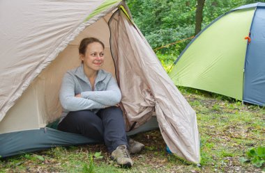 Dnepropetrovsk bölgesi, Ukrayna - 05.30. 2015: Bir çadırın yanında oturan genç bir kadın ormanın ortasında doğaya hayran. Açık hava eğlencesi konsepti. Kamp..