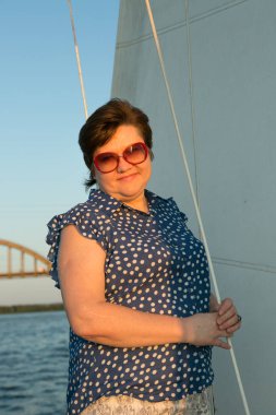 Lüks bir yat tatili. Tekne güvertesinde güneş gözlüklü mutlu orta yaşlı kadın nehirde yüzüyor..