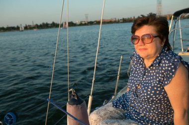 Lüks bir yat tatili. Tekne güvertesinde güneş gözlüklü mutlu orta yaşlı kadın nehirde yüzüyor..