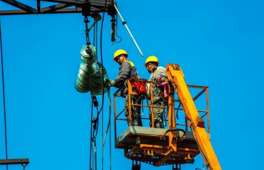 Dnepropetrovsk, Ukrayna - 08.06.2021: Vinç ve mavi gökyüzü ile yüksek voltajlı güç iletim kulesi işçileri. Patlayan asansörlerdeki hidrolik hattı çalışanları yüksek voltajlı elektrik hattı kuleleri üzerinde çalışıyorlar..