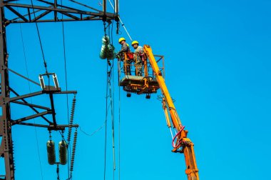 Dnepropetrovsk, Ukrayna - 08.06.2021: Vinç ve mavi gökyüzü ile yüksek voltajlı güç iletim kulesi işçileri. Patlayan asansörlerdeki hidrolik hattı çalışanları yüksek voltajlı elektrik hattı kuleleri üzerinde çalışıyorlar..