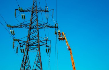 Dnepropetrovsk, Ukrayna - 08.06.2021: Vinç ve mavi gökyüzü ile yüksek voltajlı güç iletim kulesi işçileri. Patlayan asansörlerdeki hidrolik hattı çalışanları yüksek voltajlı elektrik hattı kuleleri üzerinde çalışıyorlar..