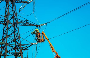 Dnepropetrovsk, Ukrayna - 08.06.2021: Vinç ve mavi gökyüzü ile yüksek voltajlı güç iletim kulesi işçileri. Patlayan asansörlerdeki hidrolik hattı çalışanları yüksek voltajlı elektrik hattı kuleleri üzerinde çalışıyorlar..