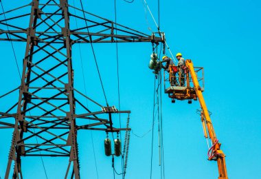 Dnepropetrovsk, Ukraine - 08.06.2021: High voltage power line transmission tower workers with crane and blue sky. Hydro linemen on boom lifts working on high voltage power line towers. clipart