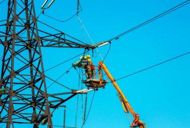 Dnepropetrovsk, Ukrayna - 08.06.2021: Vinç ve mavi gökyüzü ile yüksek voltajlı güç iletim kulesi işçileri. Patlayan asansörlerdeki hidrolik hattı çalışanları yüksek voltajlı elektrik hattı kuleleri üzerinde çalışıyorlar..