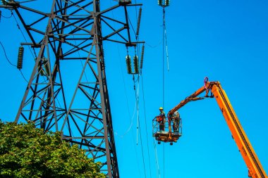 Dnepropetrovsk, Ukrayna - 08.06.2021: Vinç ve mavi gökyüzü ile yüksek voltajlı güç iletim kulesi işçileri. Patlayan asansörlerdeki hidrolik hattı çalışanları yüksek voltajlı elektrik hattı kuleleri üzerinde çalışıyorlar..