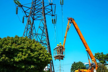 Dnepropetrovsk, Ukrayna - 08.06.2021: Vinç ve mavi gökyüzü ile yüksek voltajlı güç iletim kulesi işçileri. Patlayan asansörlerdeki hidrolik hattı çalışanları yüksek voltajlı elektrik hattı kuleleri üzerinde çalışıyorlar..