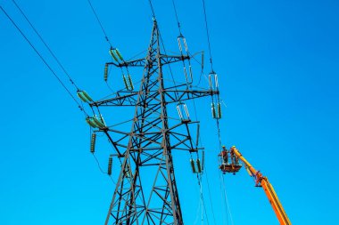 Dnepropetrovsk, Ukrayna - 08.06.2021: Vinç ve mavi gökyüzü ile yüksek voltajlı güç iletim kulesi işçileri. Patlayan asansörlerdeki hidrolik hattı çalışanları yüksek voltajlı elektrik hattı kuleleri üzerinde çalışıyorlar..