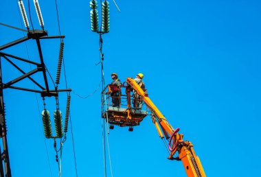Dnepropetrovsk, Ukrayna - 08.06.2021: Vinç ve mavi gökyüzü ile yüksek voltajlı güç iletim kulesi işçileri. Patlayan asansörlerdeki hidrolik hattı çalışanları yüksek voltajlı elektrik hattı kuleleri üzerinde çalışıyorlar..
