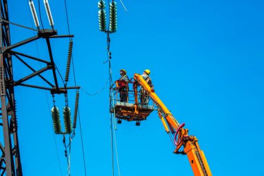 Dnepropetrovsk, Ukrayna - 08.06.2021: Vinç ve mavi gökyüzü ile yüksek voltajlı güç iletim kulesi işçileri. Patlayan asansörlerdeki hidrolik hattı çalışanları yüksek voltajlı elektrik hattı kuleleri üzerinde çalışıyorlar..