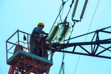 Dnepropetrovsk, Ukrayna - 08.06.2021: Vinç ve mavi gökyüzü ile yüksek voltajlı güç iletim kulesi işçileri. Patlayan asansörlerdeki hidrolik hattı çalışanları yüksek voltajlı elektrik hattı kuleleri üzerinde çalışıyorlar..