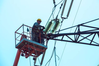 Dnepropetrovsk, Ukrayna - 08.06.2021: Vinç ve mavi gökyüzü ile yüksek voltajlı güç iletim kulesi işçileri. Patlayan asansörlerdeki hidrolik hattı çalışanları yüksek voltajlı elektrik hattı kuleleri üzerinde çalışıyorlar..