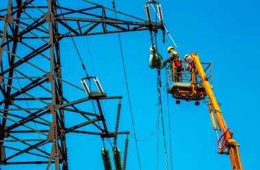 Dnepropetrovsk, Ukrayna - 08.06.2021: Vinç ve mavi gökyüzü ile yüksek voltajlı güç iletim kulesi işçileri. Patlayan asansörlerdeki hidrolik hattı çalışanları yüksek voltajlı elektrik hattı kuleleri üzerinde çalışıyorlar..