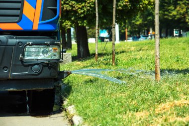 Çimleri sulamak için bir kamyon su püskürterek çimlere su döker. Şehir bahçe bakımı hizmetleri.