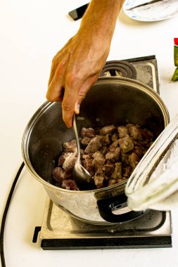 Bir kadının eli, kızarmış soğanla çiğ eti kaşıkla karıştırır. Et ve soğan pişirme süreci.