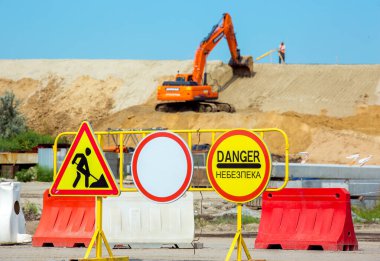 Trafik yok, inşaat işi ve tehlike yok. Tehlike kelimesi Ukraynaca yazılmış. İnşaat alanında çalışan bir buldozerin arka planında tabelalar var..