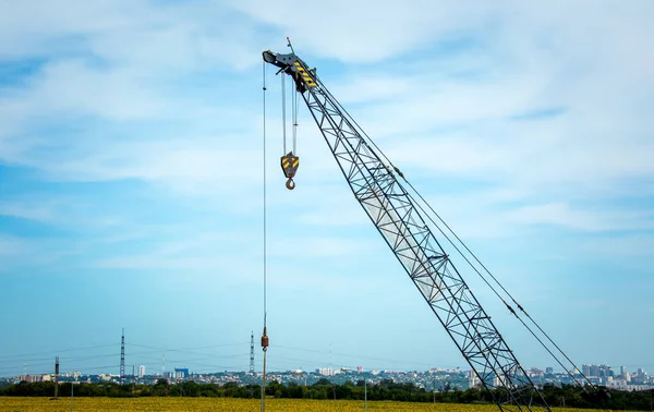 The arrow of an industrial construction crane on the background of the blue sky and panorama of the city. Construction of a bypass road.