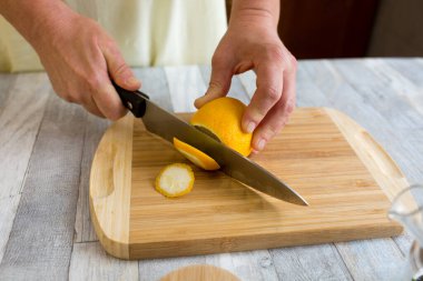 Bir kadın, ahşap mutfak tahtasındaki limonu keskin büyük bir bıçakla kesiyor. Sağlıklı gıda konsepti. Naneli ve limonlu çay yapma süreci.
