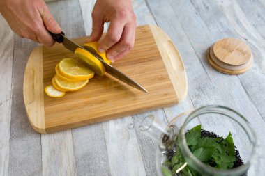 Bir kadın, ahşap mutfak tahtasındaki limonu keskin büyük bir bıçakla kesiyor. Sağlıklı gıda konsepti. Naneli ve limonlu çay yapma süreci.