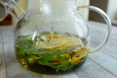Bir kadın nane, çay ve dilimlenmiş limonla çaydanlığa sıcak su döker. Naneli ve limonlu çay yapma süreci. Sağlıklı gıda konsepti.