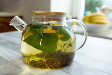 Masadaki cam çaydanlıkta naneli çay, çay ve dilimlenmiş limon. Naneli ve limonlu çay yapma süreci. Sağlıklı gıda konsepti.