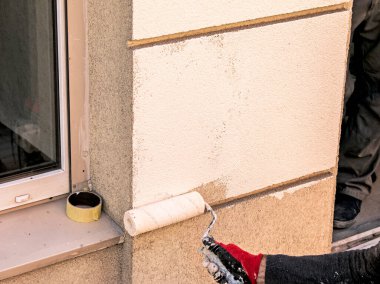 Tekerlekli bir erkek el, duvarı bej boyayla boyuyor. Binanın dış duvarını kışa hazırlıyorum..