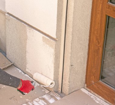 Tekerlekli bir erkek el, duvarı bej boyayla boyuyor. Binanın dış duvarını kışa hazırlıyorum..