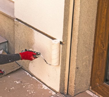 Tekerlekli bir erkek el, duvarı bej boyayla boyuyor. Binanın dış duvarını kışa hazırlıyorum..