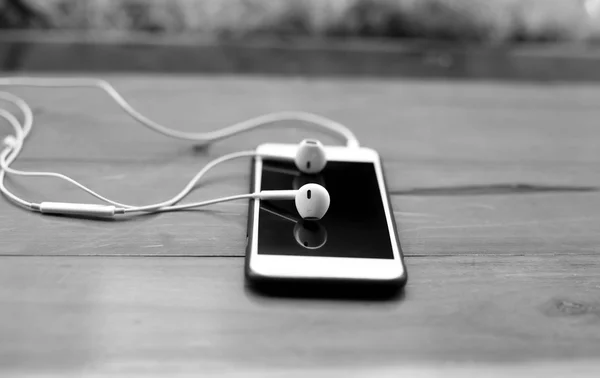 Cell phone and eare phone on wooden table — Stock Photo, Image