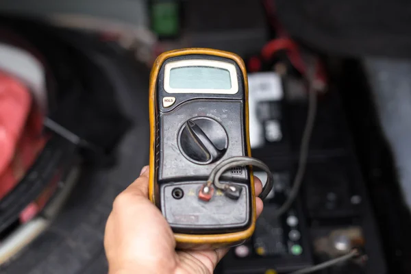 Mecânico verificando o nível da bateria de um carro com voltímetro — Fotografia de Stock