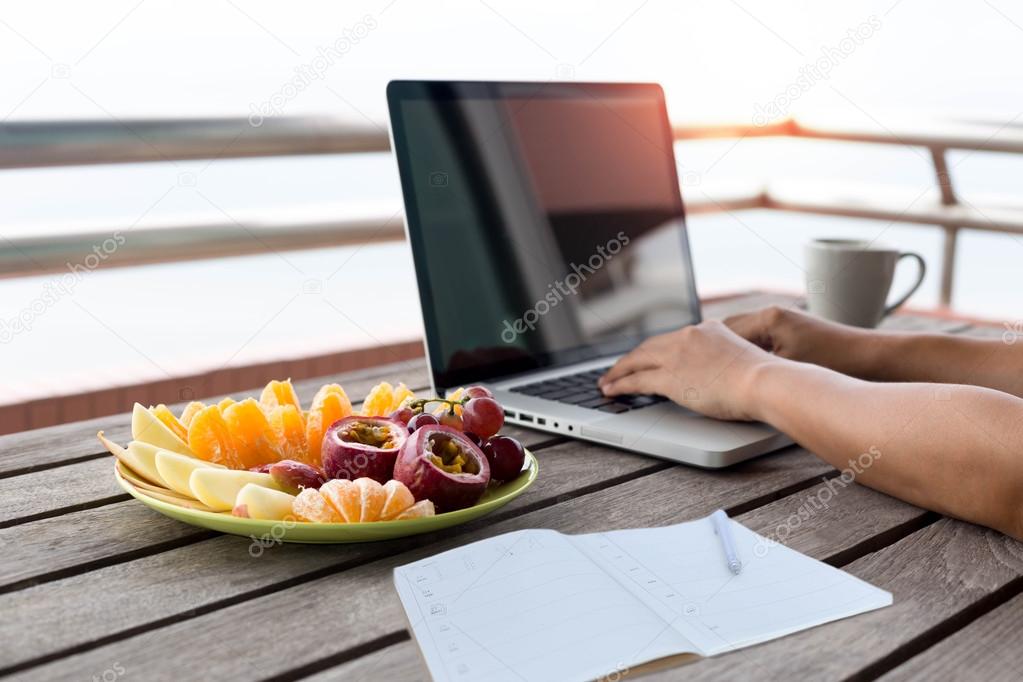 Fresh fruit with man working on laptop and notebook with pen in 