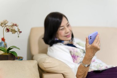 Seçilmiş odak mutlu son sınıf kadın video görüşmesi için telefon kullanarak koltukta oturuyor