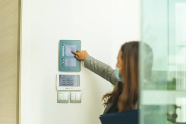 Koruyucu maskeli kadın emlakçı. Güvenlik ekranını işaret ediyor.