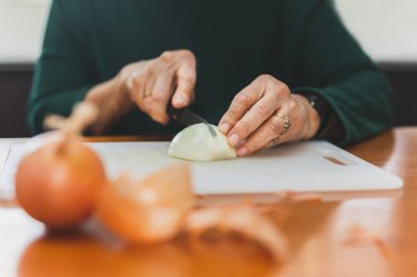 Yaşlı kadının elleri soğanları bıçakla kesiyor..