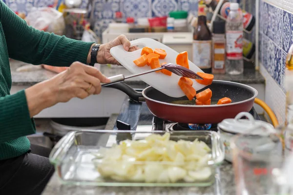 Senior woman putting carrots in frirying pan. — Stock fotografie