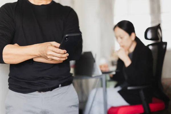 Üzletember használja a mobiltelefon, míg a nő dolgozik a háttérben. — Stock Fotó