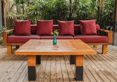 Bahçedeki ahşap zeminde kırmızı yastıklı ahşap masa ve kanepe.
