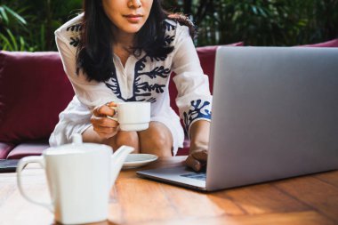 Kadın tatilde dizüstü bilgisayarını kullanarak sabah kahvesinden zevk alıyor..