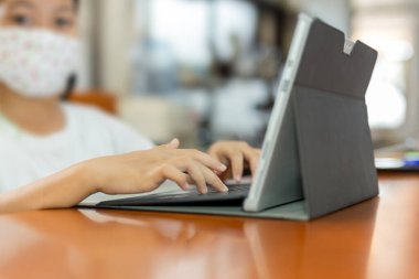 Koruyucu maskeli genç bir öğrenci dizüstü bilgisayarda yazı yazıyor..