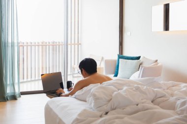 Dizüstü bilgisayarda çalışan adam tatilde yatakta yatıyor..