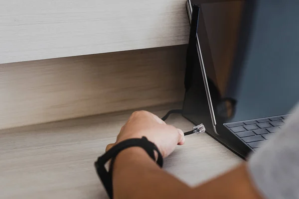 Man hand connecting internet cable wire to laptop.