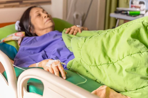 Mano de paciente mayor con solución salina inyectable acostada en la cama del hospital. — Foto de Stock