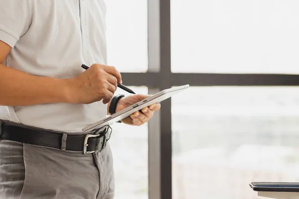 Zakenman staat naast het raam in zijn kantoor met digitale tablet. — Stockfoto