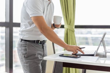 İş adamı dizüstü bilgisayarda e-postaları kontrol ediyor ve elinde fincan kahve tutuyor..