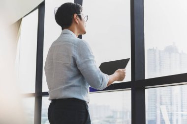 İş adamı ofis penceresinin yanında dururken dijital tablet tutuyor.