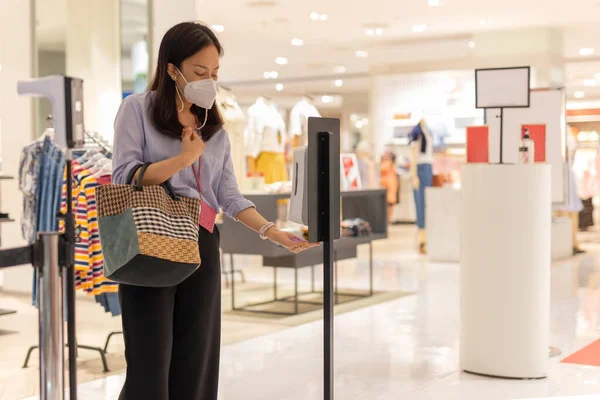 Kobieta w masce ochronnej przy użyciu automatycznego żelu alkoholowego na ręce przed wejściem do centrum handlowego. — Zdjęcie stockowe