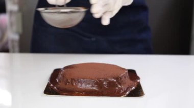 Kadın fırıncı kakao tozuyla çikolatalı pasta pudralıyor..